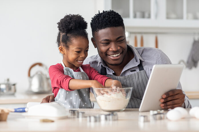 Adorable Black Father And Daughter Baking Together, Using Digita