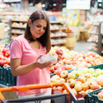Food at Home Prices Drop for the First Time Since 2020: March CPI Report Young Brunette Woman Picks Chooses Fruits On The Counter In Supe