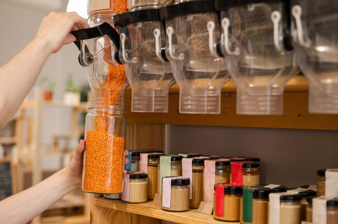A Man Fills A Jar With Red Lentils. Selling Bulk Goods By Weight