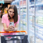 How Can the Food and Beverage Industry Enhance Gen Z Customer Satisfaction? Happy Caucasian Woman Using Mobile Phone In Grocery Shopping. Ch
