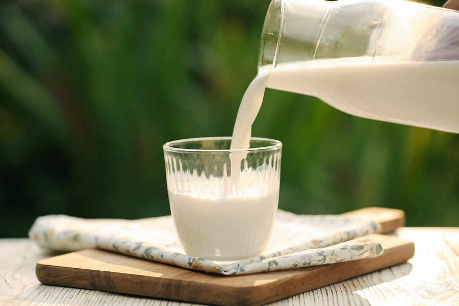 Pouring Tasty Fresh Milk From Bottle Into Glass On White Wooden