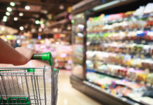 General Mills Repriced Two-Thirds of Its Portfolio and Still Lost Volume. Here’s What’s Really Growing Units. Woman Hand Hold Supermarket Shopping Cart With Abstract Grocery