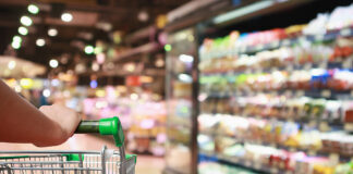 General Mills Repriced Two-Thirds of Its Portfolio and Still Lost Volume. Here’s What’s Really Growing Units. Woman Hand Hold Supermarket Shopping Cart With Abstract Grocery