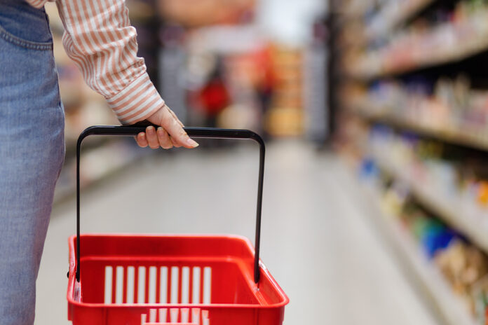 Female Hand Holds Empty Red Grocery Cart, Close-up. In Backgroun