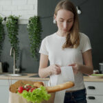 Student Loan Forbearance Is Ending: What Food Industry Executives Need to Know Young Woman With A Bag Of Groceries Checks And Examines A Produc