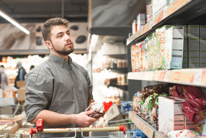 Man With A Beard Stands In A Supermarket With A Pack In His Hand
