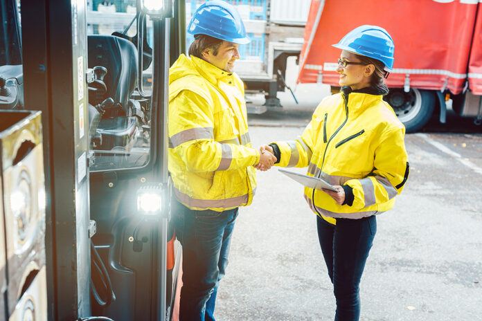 Worker and manager shaking hands at distribution center behind a