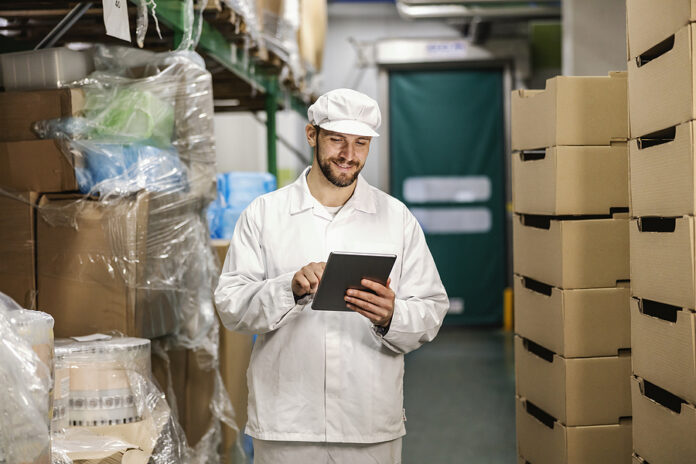 A Food Factory Worker Is Scrolling On Tablet In Storage.