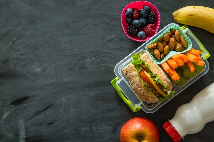 School lunch box with books and pencils in front of black board, copy space